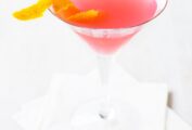 A Cosmopolitan cocktail in a martini glass with a twist of orange peel floating in it.