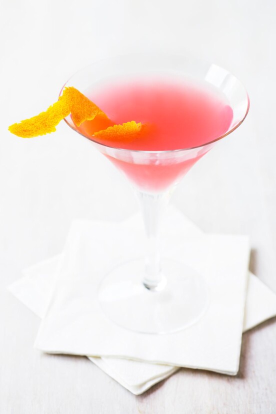 A Cosmopolitan cocktail in a martini glass with a twist of orange peel floating in it.