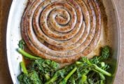 A large coil of Italian sausage and broccoli rabe in an oval skillet.