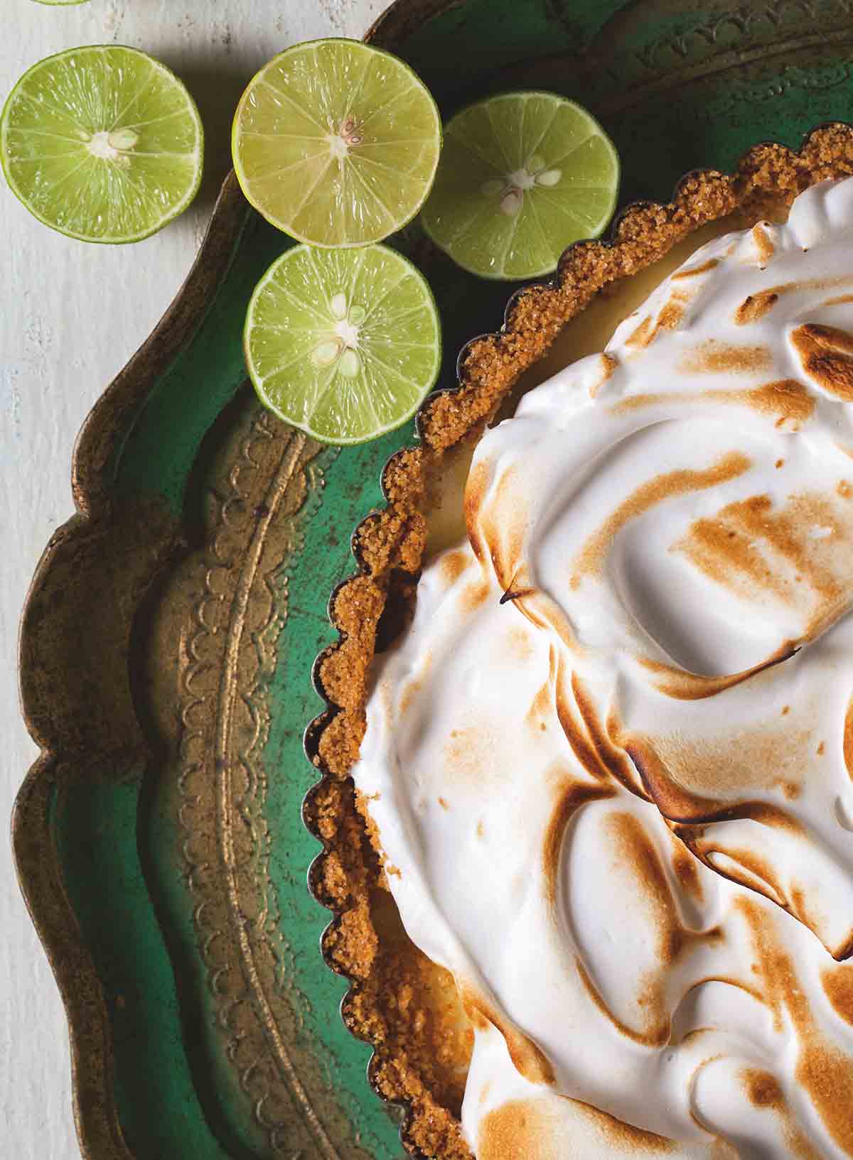 A classic key lime pie with a meringue top and several sliced limes nearby