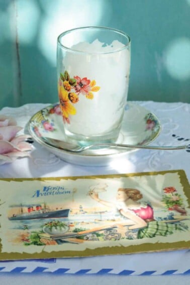 A glass filled with ouzo sorbet in a small china dish with a spoon resting beside it.