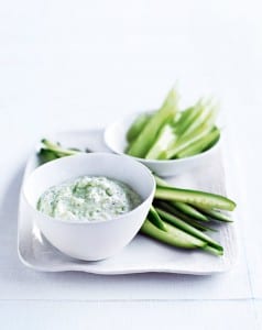 A white platter with sliced celery and cucumber and a white bowl of feta dip on top.
