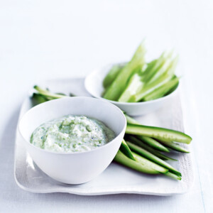 A white platter with sliced celery and cucumber and a white bowl of feta dip on top.