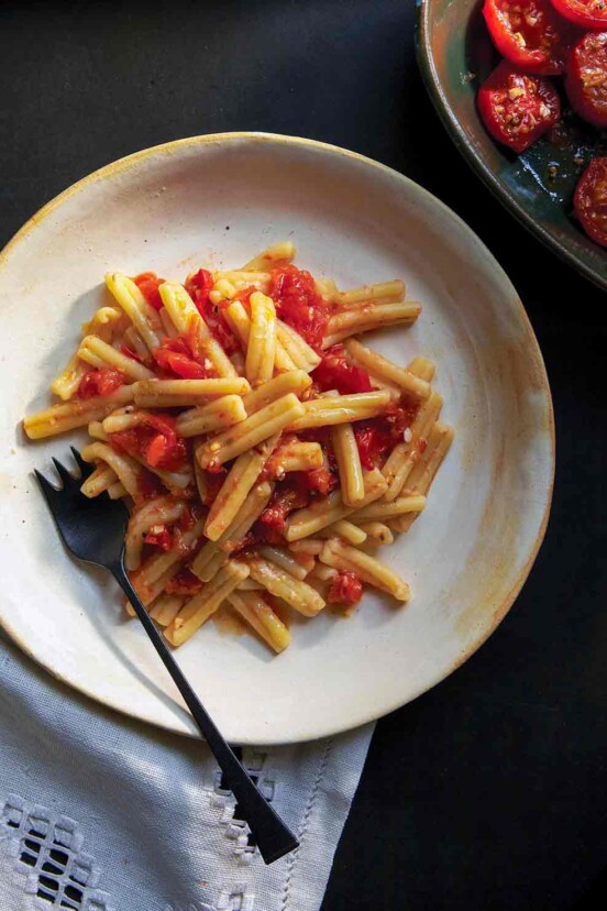 A white plate with cavatelli past topped with a roasted tomato sauce, fork on the side