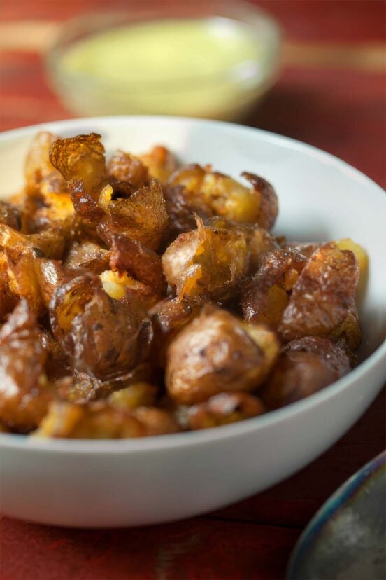 A white bowl filled with smoked pickled potatoes with anchovy aioli in a bowl on the side.