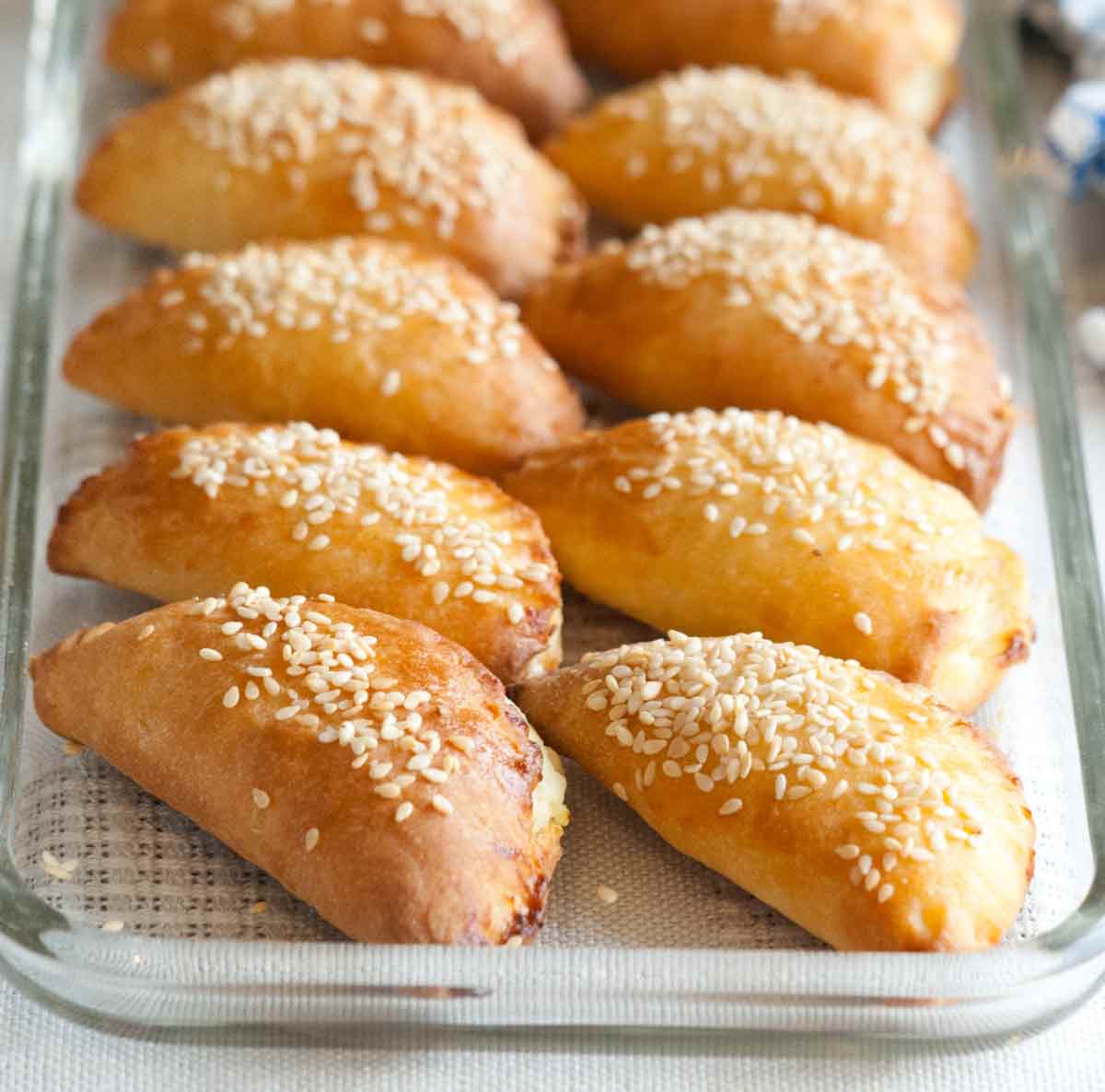 Ten Turkish borekitas sprinkled with sesame seeds in a glass baking dish