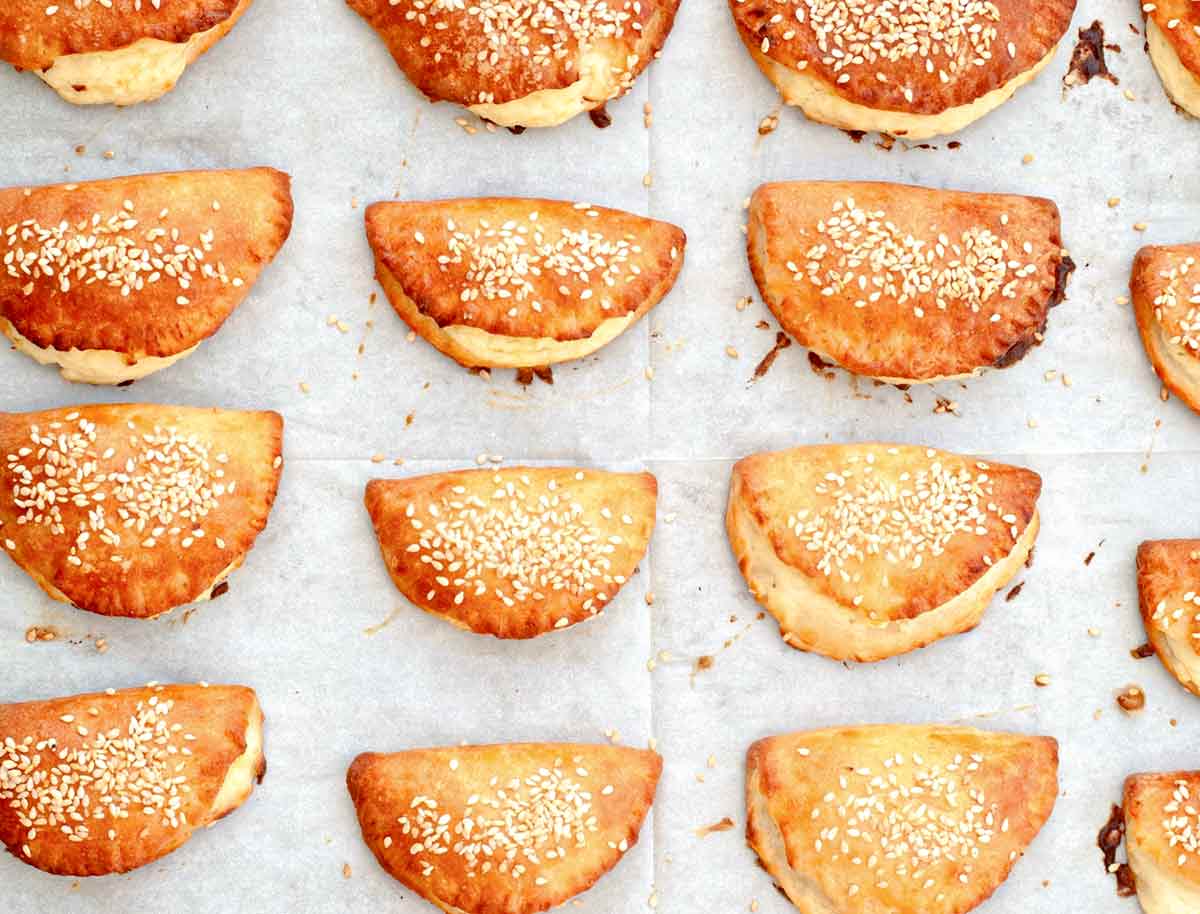 Twelve Turkish borekitas sprinkled with sesame seeds on a piece of parchment.