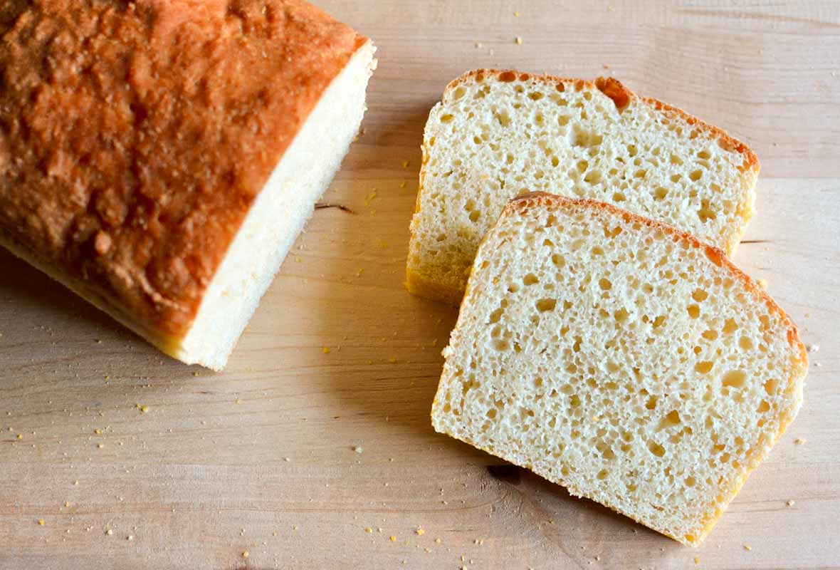 A loaf of English muffin bread with two slices cut from the end on a wooden board.