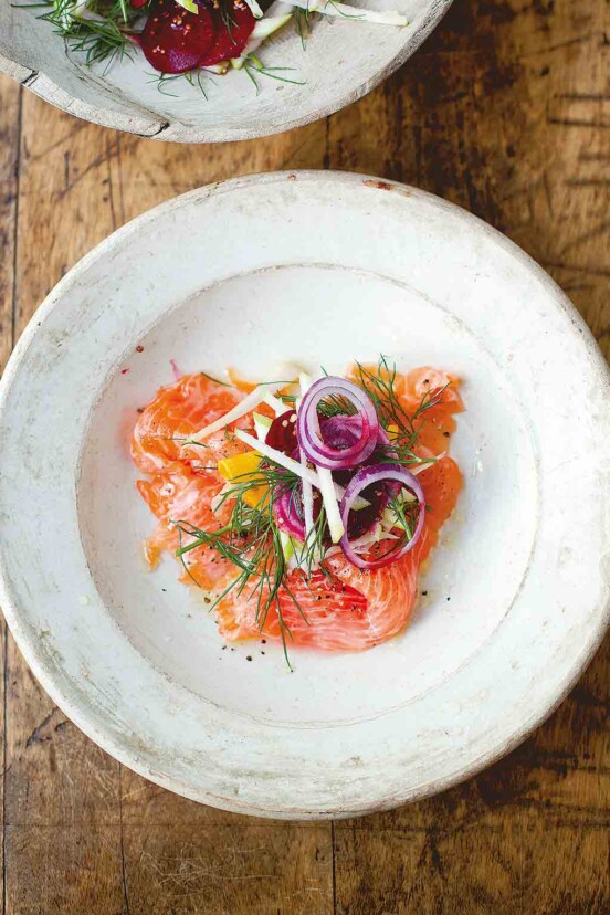 A white plate with salmon, fennel, and apple salad topped with red onion and dill.