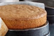 A spiced nut cake resting on an upside-down cake pan with a strip of parchment half removed from the edges of the cake.