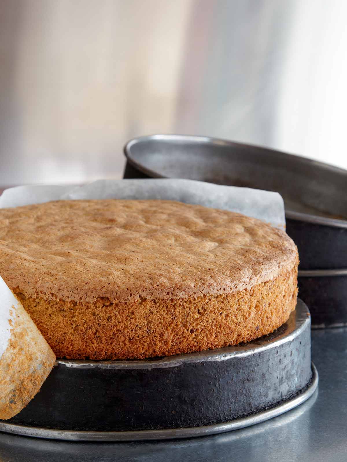 A spiced nut cake resting on an upside-down cake pan with a strip of parchment half removed from the edges of the cake.