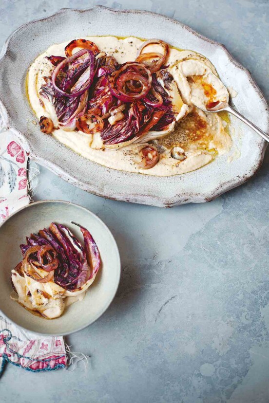 An oval platter filled with white bean puree, radicchio, and red onions with a spoon resting in it and a serving in a bowl beside.