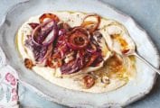 An oval platter filled with white bean puree, radicchio, and red onions with a spoon resting in it and a serving in a bowl beside.