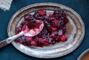 A pewter platter with chunky red apple cranberry sauce with a serving spoon