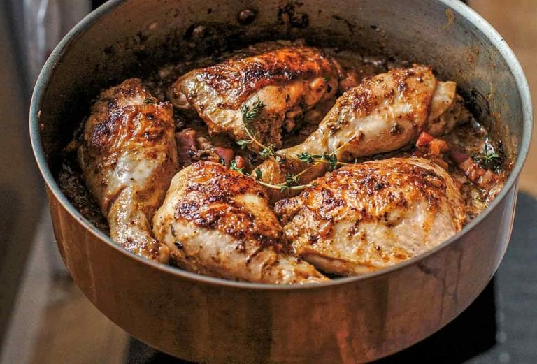 Chicken with mustard in a large metal skillet garnished with thyme.