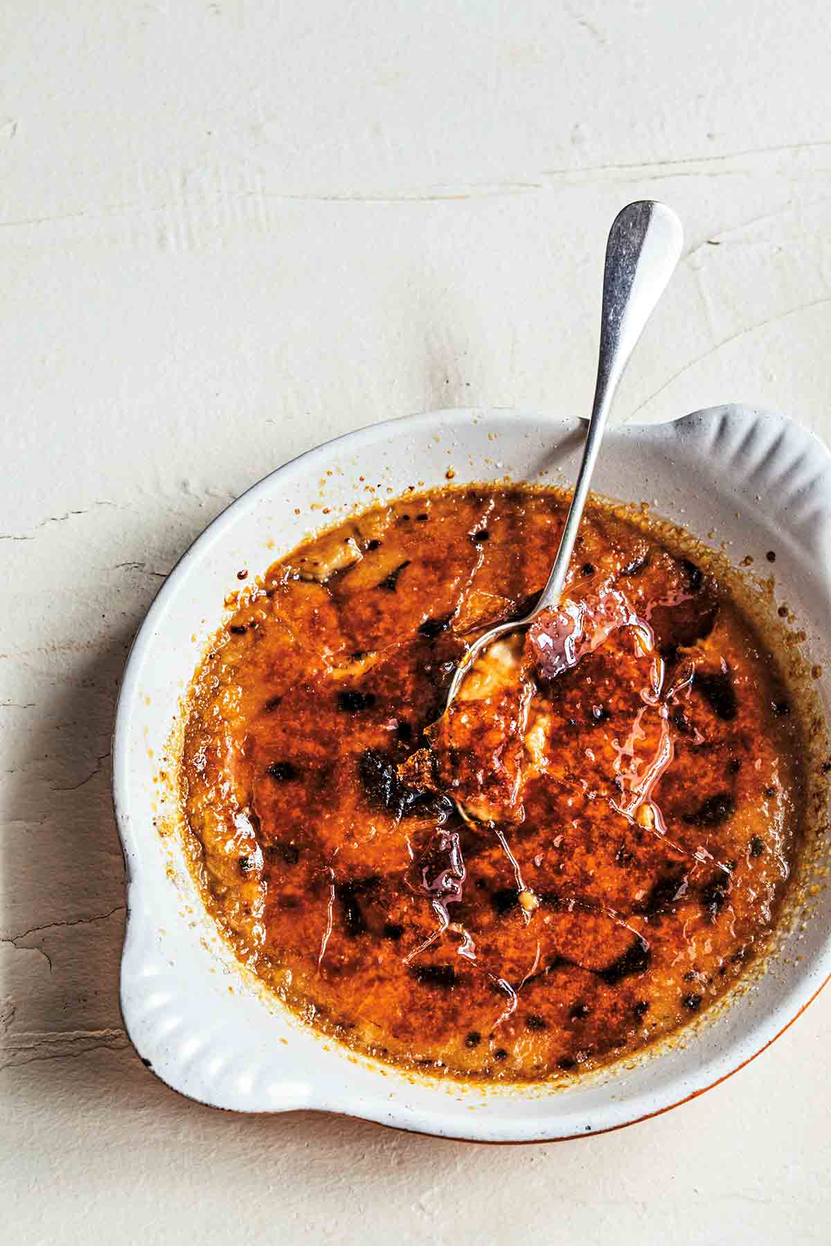 A shallow white dish filled with coffee creme brulee, with a spoon resting inside.