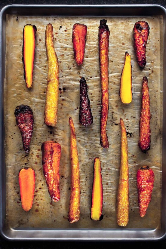 A parchment-line rimmed baking sheet with fifteen whole duck fat roasted carrots.