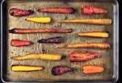 A parchment-line rimmed baking sheet with fifteen whole duck fat roasted carrots.