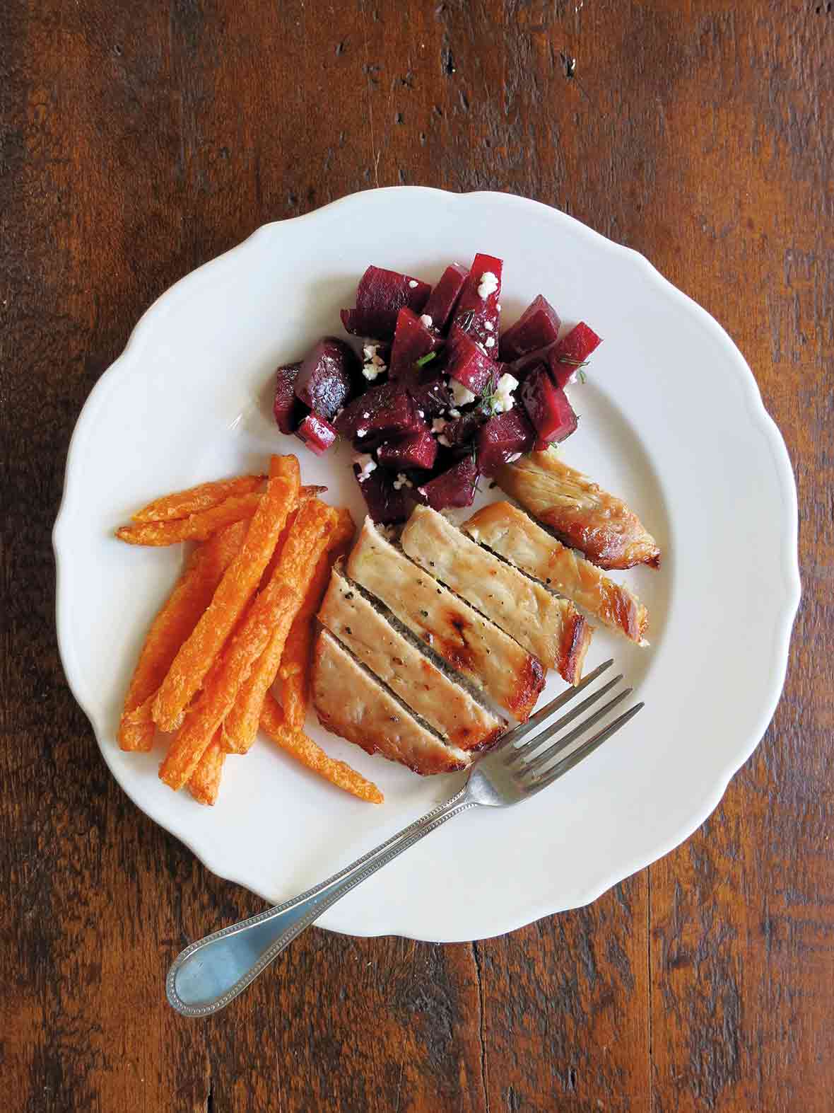 White plate with a maple pork chops, carrots, and beets with feta cheese