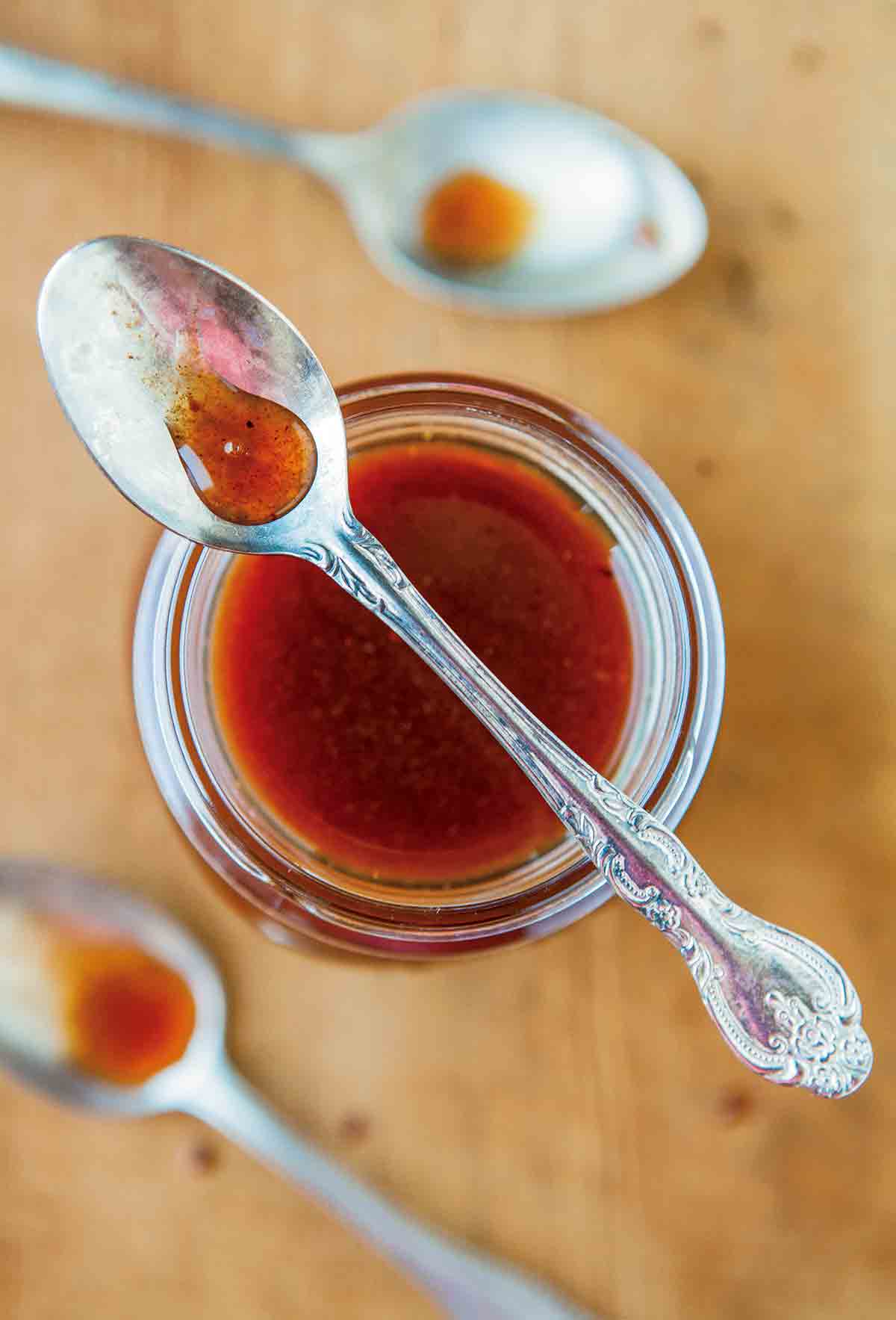 A jar of pumpkin spice syrup with a spoon resting on top and two spoons beside the jar.