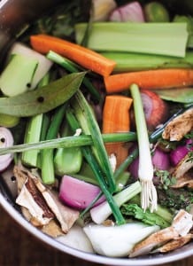 The ingredients for vegetable broth, including carrots, celery, bay leaves, and onions, in an enamel pot.