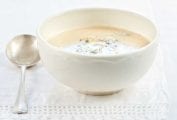 A white bowl of cauliflower soup on a white linen cloth with a spoon resting beside it.