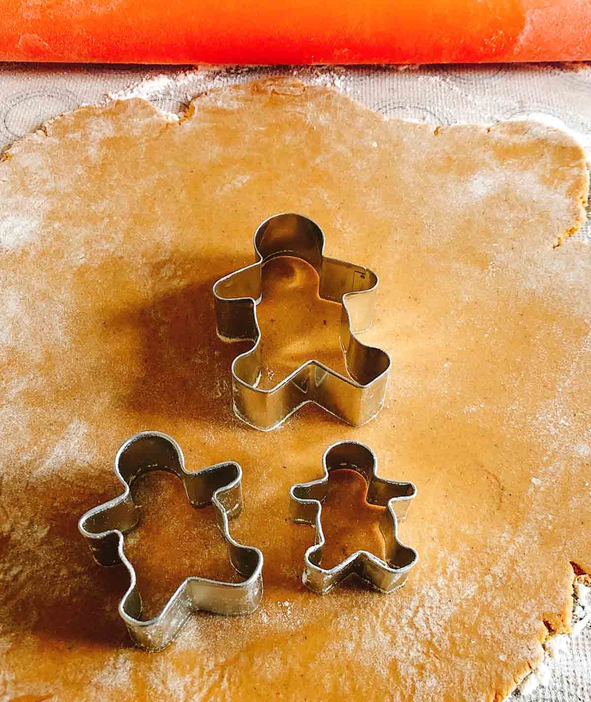 Gingerbread cookie dough rolled out on with three gingerbread men cookie cutters on top.