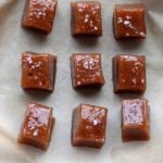 Nine square caramels topped with sea salt sitting on a sheet of parchment.