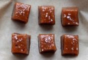 Six square caramels topped with sea salt sitting on a sheet of parchment.