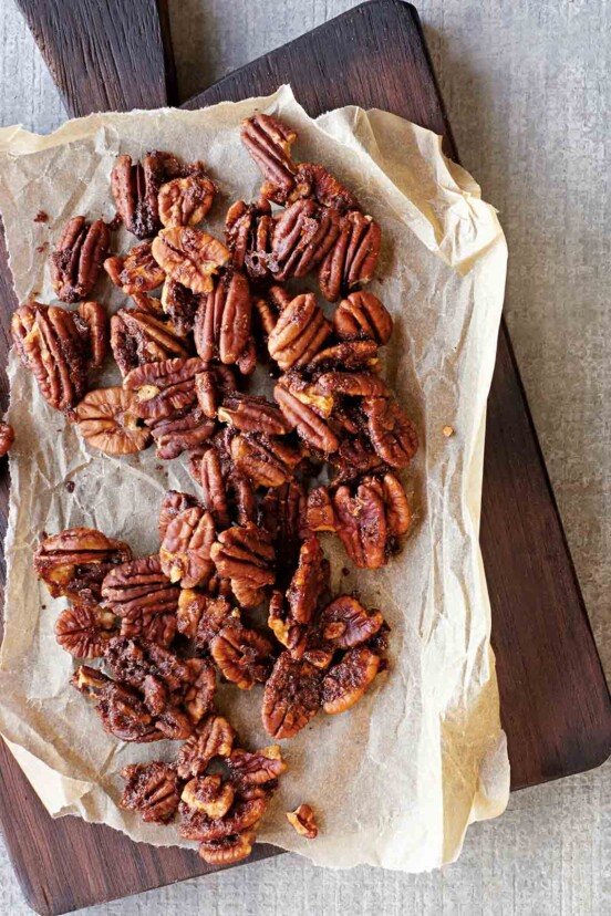Baked spiced pecans on a sheet of parchment that is resting on a wooden serving board.