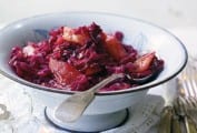 A white bowl filled with spiced red cabbage set on white linens with a spoon resting inside.