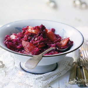 A white bowl filled with spiced red cabbage set on white linens with a spoon resting inside.