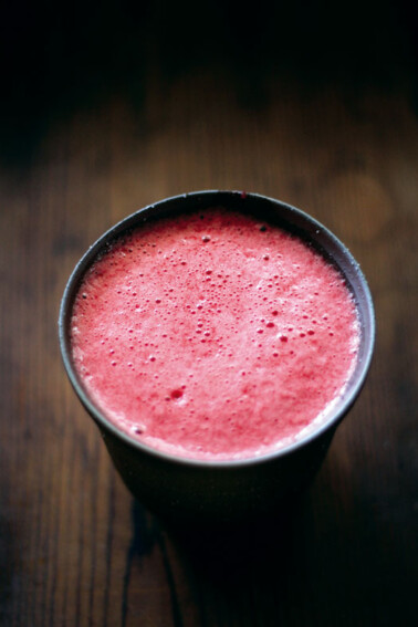 Frothy beet juice in a dark cup on a wooden table.