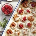 A white tray filled with Swedish meatballs--a combination of veal, pork, and beef--filled with cranberry sauce and topped with a white cream sauce