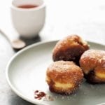 Three German Berliners, or jelly doughnuts, with raspberry jam spilling out on a plate with a cup of coffee