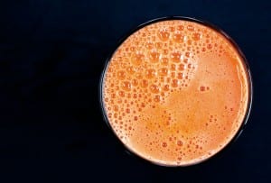 A frothy glass of carrot apple juice against a dark background