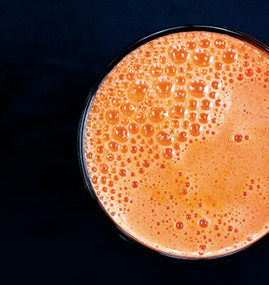 A frothy glass of carrot apple juice against a dark background