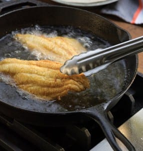 Southern fried catfish being fried in a cast-iron skillet