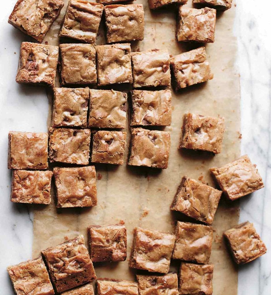 Squares of blondies with chocolate chips on parchment paper on a marble slab