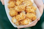 Two hands holding a paper container of tater tots sprinkled with Parmesan cheese