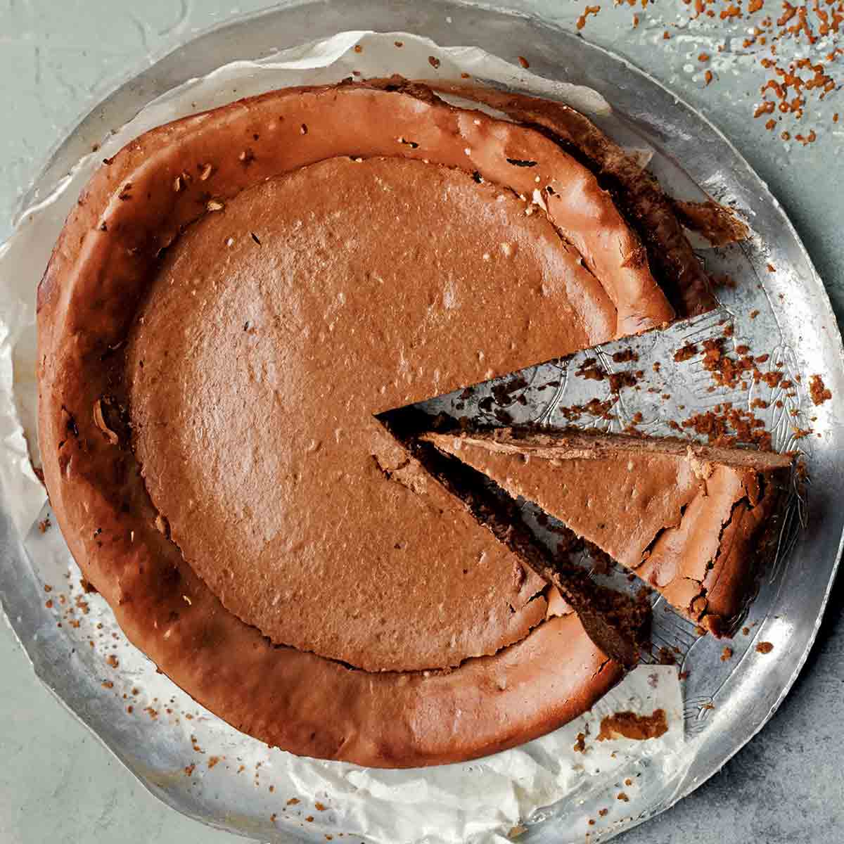 An espresso cheesecake on a silver platter with two slices cut from it.