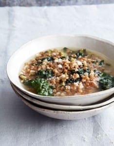 Three stacked white bowls and the top one filled with greens and grains soup, and finished with Parmesan.