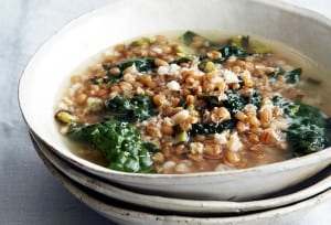 Three stacked white bowls and the top one filled with greens and grains soup, and finished with Parmesan.