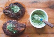 Two steaks on a cutting board topped with herbed compound butter an a bowl of the butter on the side.