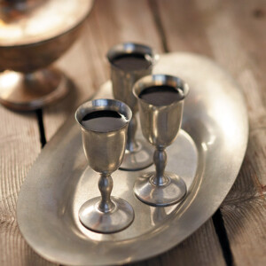 Three silver goblets of honey healer sitting on a silver tray on a wooden table.