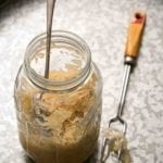 A glass jar of single quart sauerkraut with a spoon inside and a two-pronged fork lying beside it.