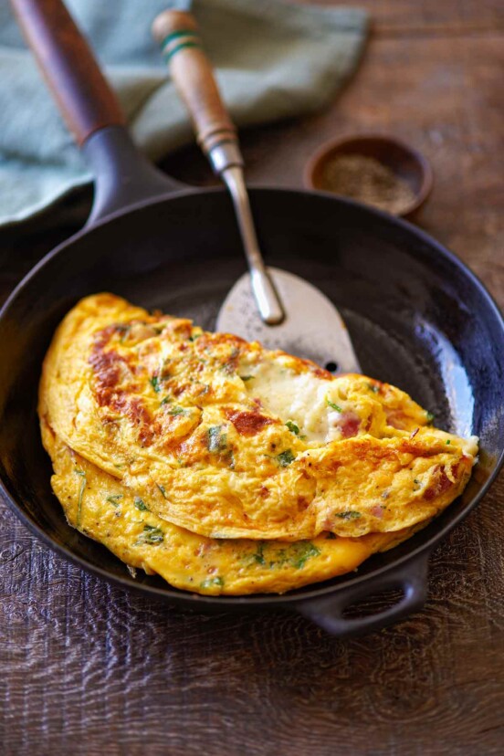 A cooked ham and cheese omelet in a small skillet with a spatula sliding underneath to flip it.