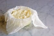 A glass bowl lined with cheesecloth, filled with some draining homemade mascarpone.