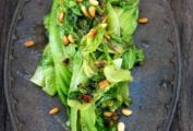 An iron plate with a pile of sautéed romaine lettuce topped with toasted pine nuts
