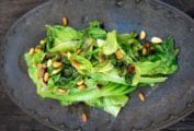 An iron plate with a pile of sautéed romaine lettuce topped with toasted pine nuts
